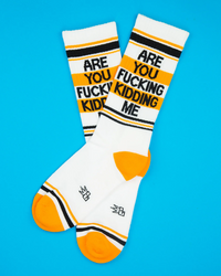 Are You Fucking Kidding Me funny gym socks in white with orange toes, black lettering and retro stripes displayed as a pair on blue background