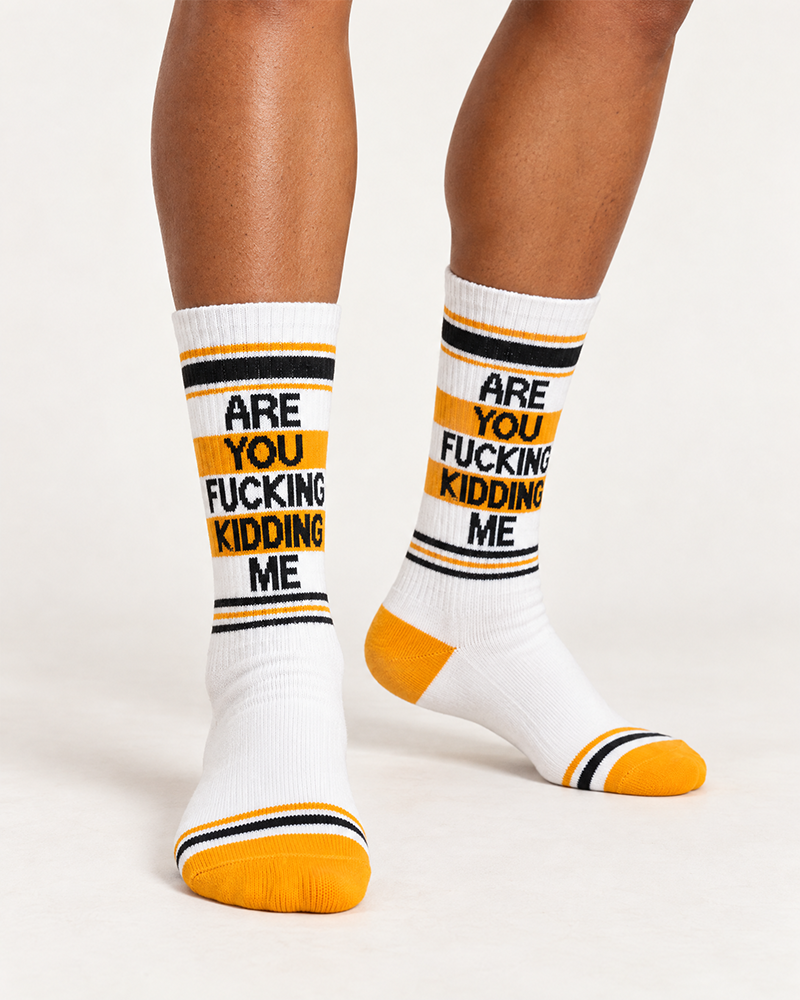 Female model wearing Are You Fucking Kidding Me white crew socks with bold black text and orange accents, made in USA