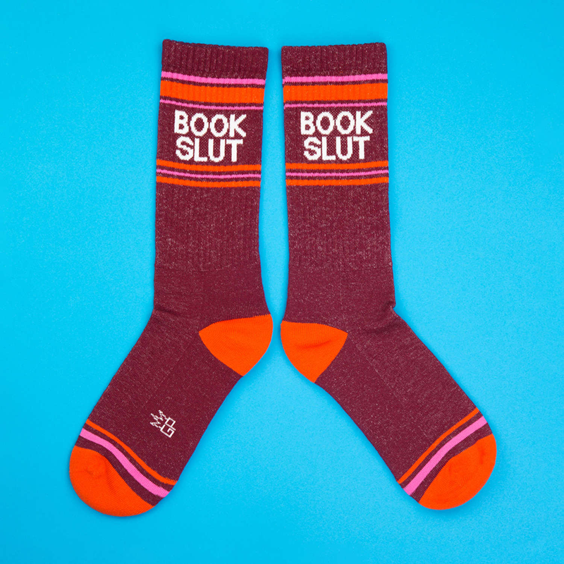 Pair of burgundy Book Slut novelty socks with white text, orange heels and toes, and pink striped details