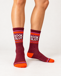Female model wearing burgundy Book Slut gym socks with white lettering, pink stripes and orange toes