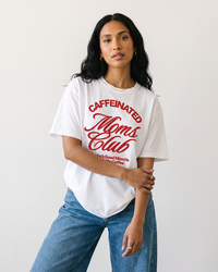 Woman wearing white Caffeinated Moms Club coffee mom graphic tee with blue jeans