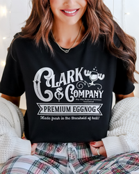 Close-up of black Clark & Company Premium Eggnog graphic tee styled with plaid holiday pajama pants.