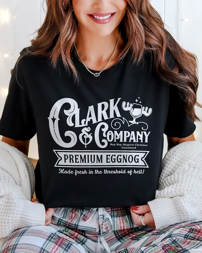 Close-up of black Clark & Company Premium Eggnog graphic tee styled with plaid holiday pajama pants.