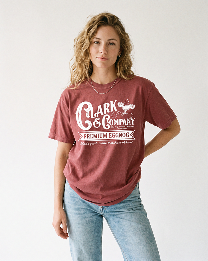 Blonde woman wearing a brick red Clark & Company Eggnog heavyweight Christmas graphic tee with light wash jeans.