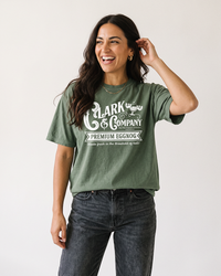 Dark-haired woman wearing a hemp green Clark Griswold-inspired Christmas graphic t-shirt with black jeans.