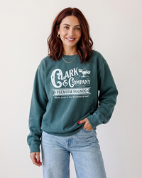 Auburn-haired woman wearing a Blue Spruce green heavyweight Christmas graphic sweatshirt with light wash jeans.