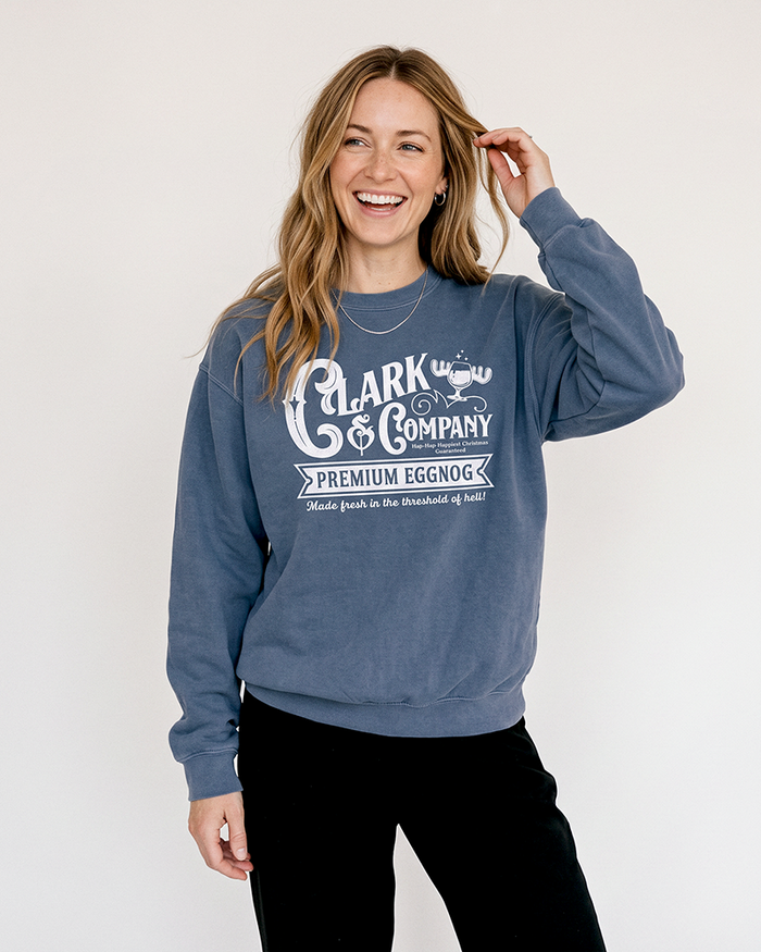 Blonde woman wearing a denim blue Clark Griswold-inspired Christmas crewneck sweatshirt with black pants.