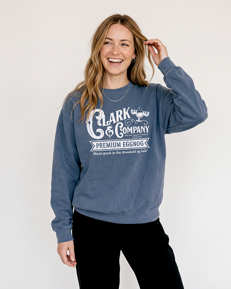 Blonde woman wearing a denim blue Clark Griswold-inspired Christmas crewneck sweatshirt with black pants.