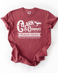 Brick red Comfort Colors heavyweight Christmas tee featuring a white Clark & Company Premium Eggnog graphic and moose mug illustration.