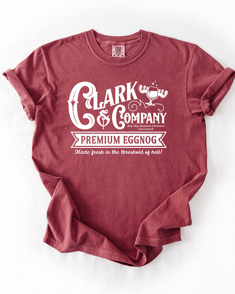 Brick red Comfort Colors heavyweight Christmas tee featuring a white Clark & Company Premium Eggnog graphic and moose mug illustration.