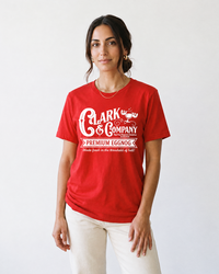 Woman wearing a red Clark & Company Premium Eggnog Christmas movie graphic tee with white pants.