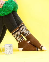Model wearing brown Coffee Makes Me Poop gym socks with retro stripes beside a coffee mug