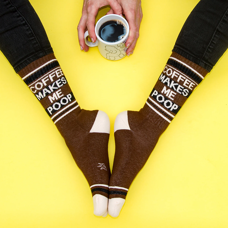 Brown Coffee Makes Me Poop novelty crew socks worn with black jeans and a cup of coffee