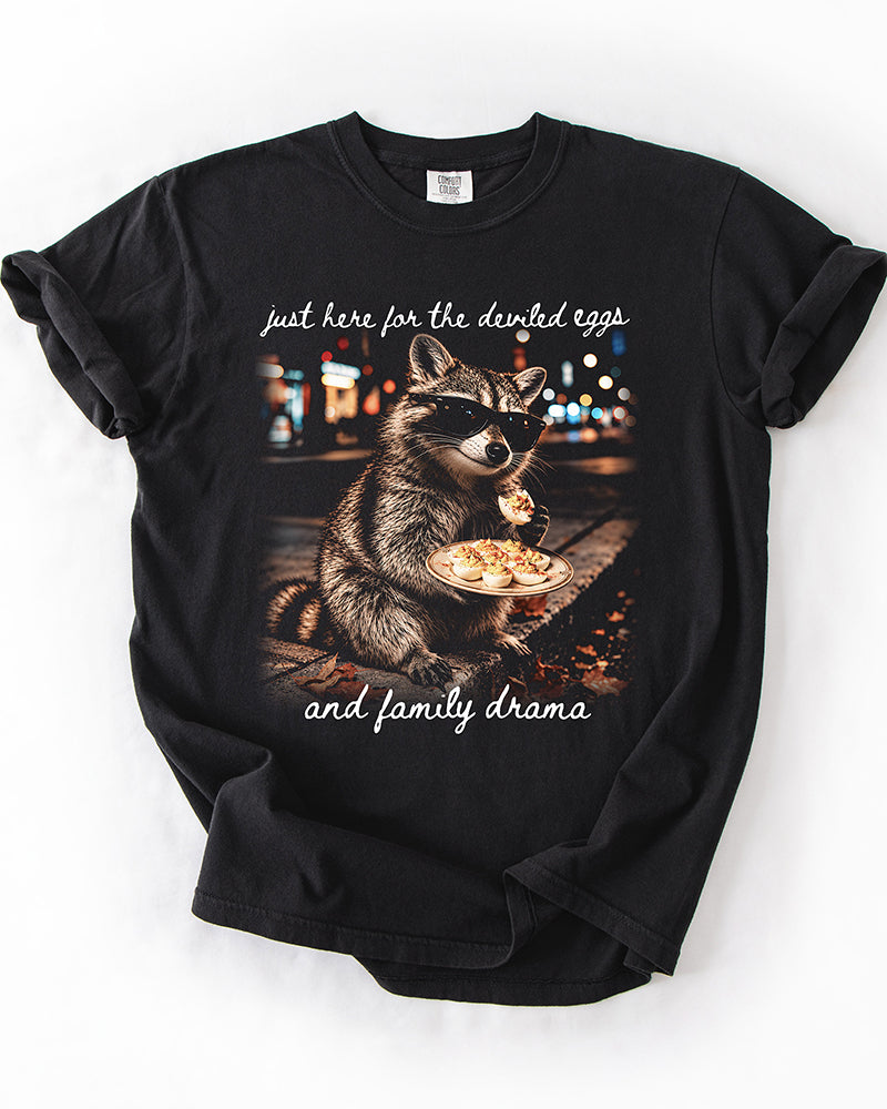 Black Comfort Colors heavyweight tee with funny raccoon and deviled eggs artwork and white family drama script lettering.