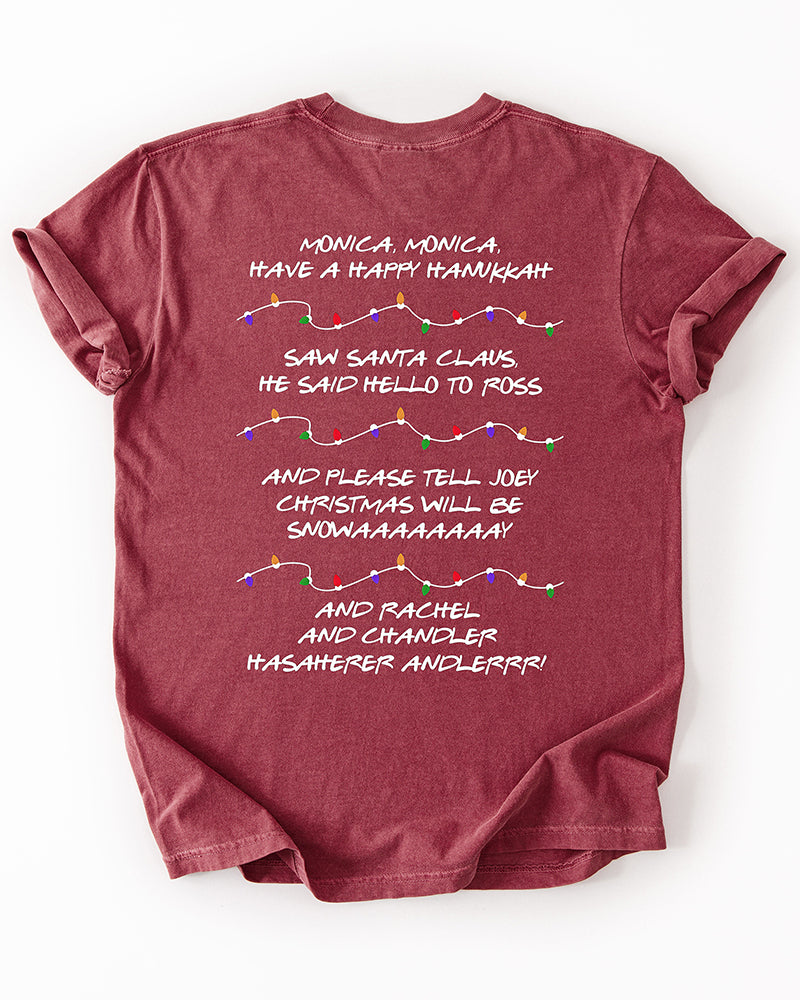 Back of brick red Friends Christmas T-shirt featuring nostalgic holiday song lyrics and illustrated strands of colorful Christmas lights.