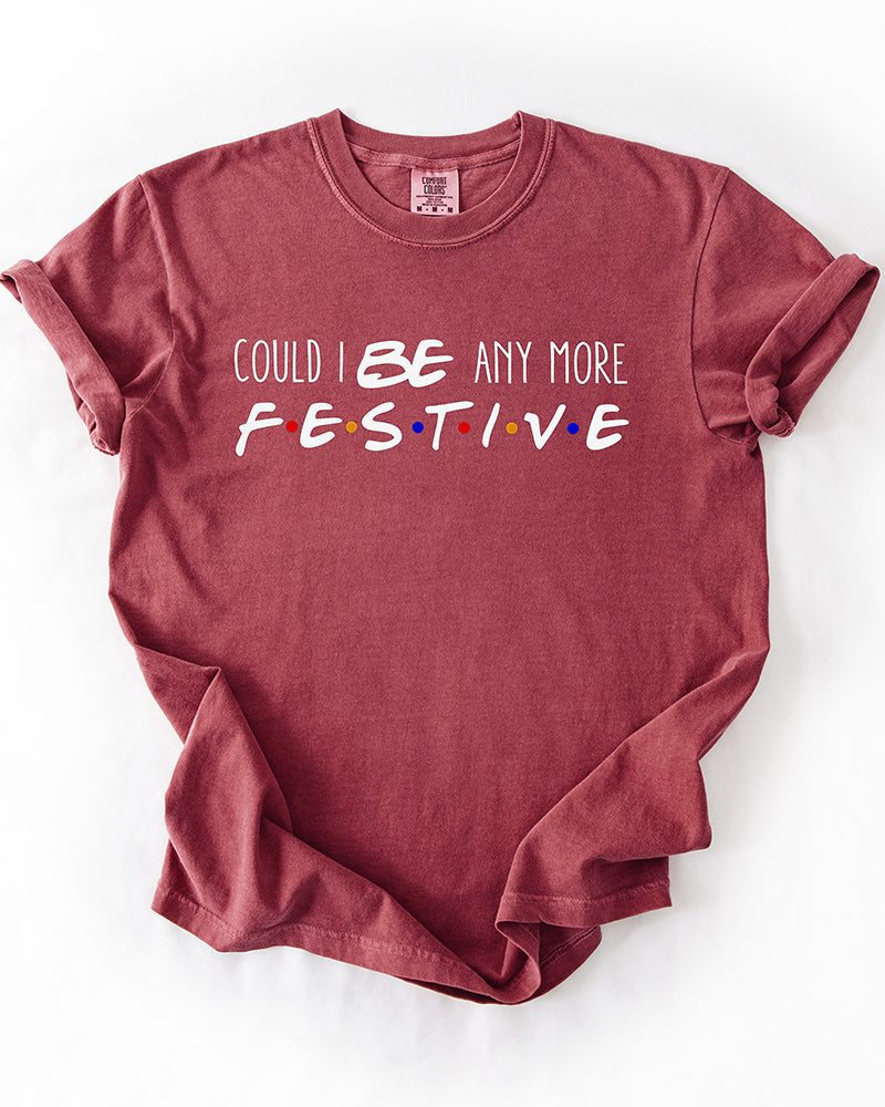 Brick red Could I Be Any More Festive heavyweight graphic tee featuring playful white lettering and multicolored dots inspired by Friends.