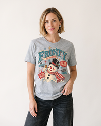 Woman wearing an Athletic Heather Frosty the Snowman vintage Christmas lightweight tee with distressed retro holiday graphic and dark jeans.