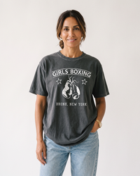 Brunette woman wearing a Pepper gray Girls Boxing heavyweight graphic tee with light-wash jeans.
