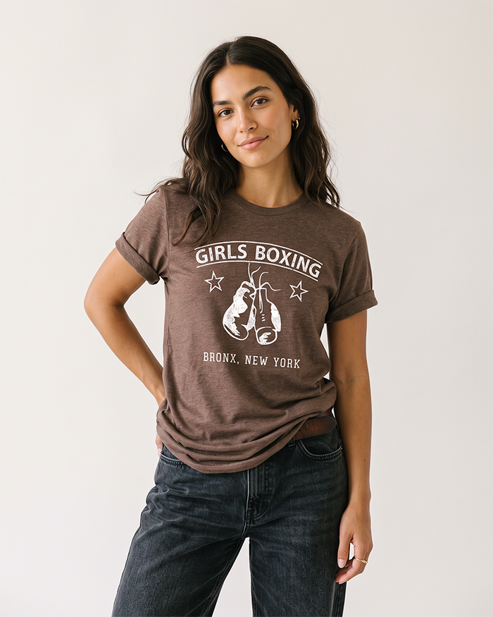 Brunette woman wearing a Heather Brown Girls Boxing tee with black jeans.