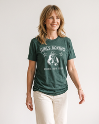Blonde woman wearing a Heather Forest Girls Boxing lightweight graphic tee with cream pants.