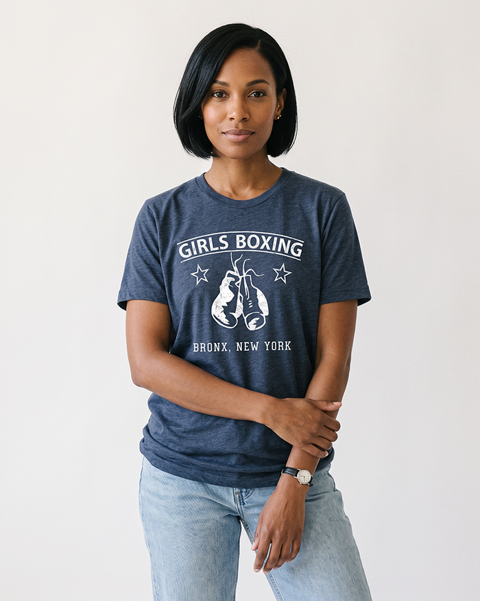 Woman with a black bob wearing a Heather Navy Girls Boxing tee with light-wash jeans.