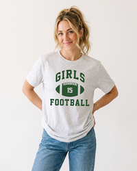 Blonde woman wearing an Ash Girls Football lightweight tee with forest green collegiate graphic and blue jeans.