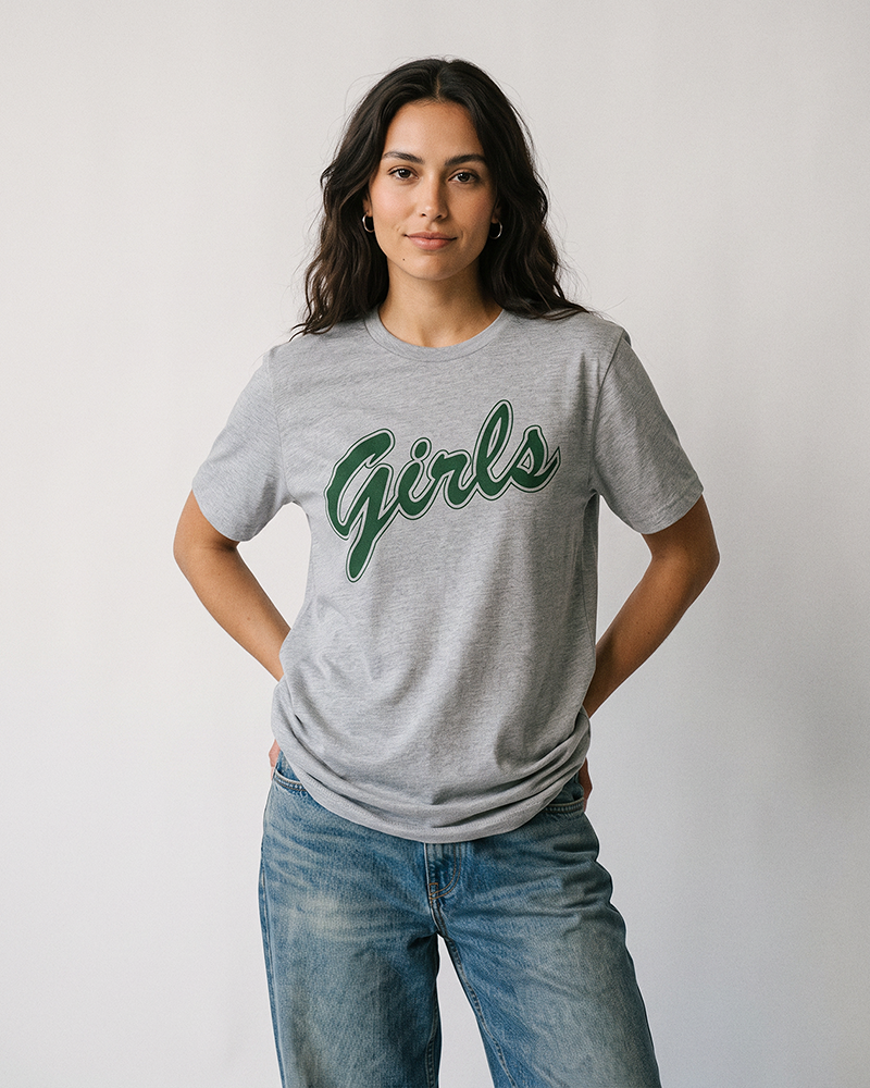 Woman wearing a lightweight heather grey Girls graphic t-shirt with forest green lettering and relaxed blue jeans.