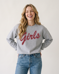 Blonde woman wearing a sport grey Girls graphic crewneck sweatshirt with rose-red lettering and blue jeans.