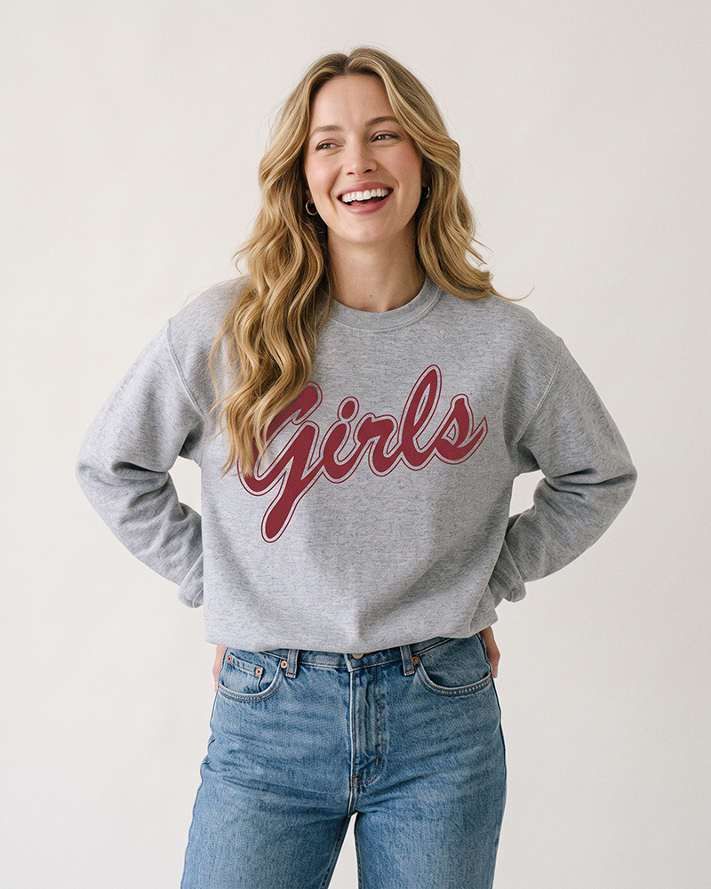 Blonde woman wearing a sport grey Girls graphic crewneck sweatshirt with rose-red lettering and blue jeans.