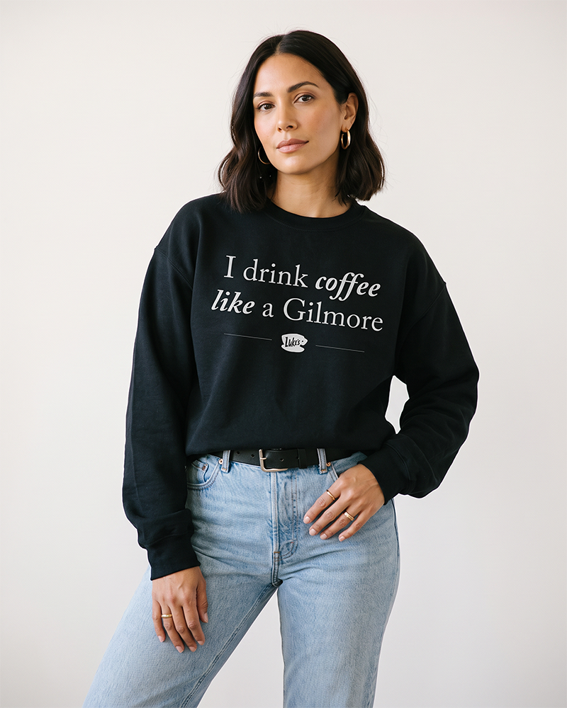 Woman wearing black I Drink Coffee Like a Gilmore sweatshirt with jeans and Luke’s coffee cup graphic