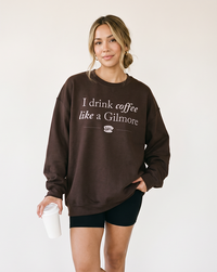 Woman holding coffee while wearing dark chocolate I Drink Coffee Like a Gilmore crewneck sweatshirt