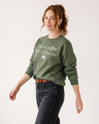 Woman wearing military green I Drink Coffee Like a Gilmore crewneck sweatshirt inspired by Gilmore Girls and Stars Hollow