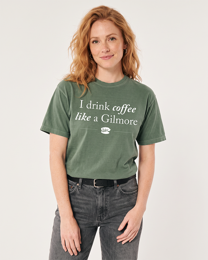 Woman wearing moss green I Drink Coffee Like a Gilmore graphic tee