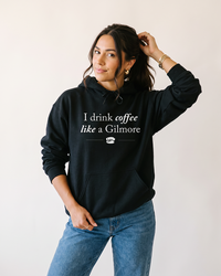 Woman wearing black I Drink Coffee Like a Gilmore hoodie inspired by Luke's Diner and Stars Hollow