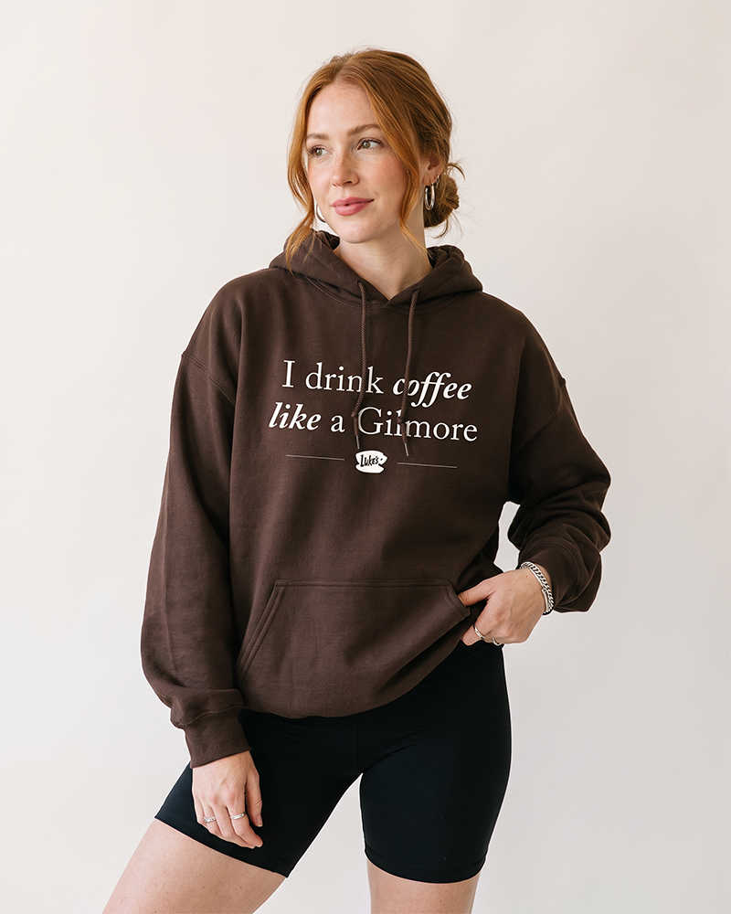 Woman wearing dark chocolate Gilmore Girls coffee hoodie with I Drink Coffee Like a Gilmore graphic