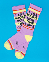 Funny book lover crew socks in lilac with bold I Like Books More Than People lettering and colorful retro stripes