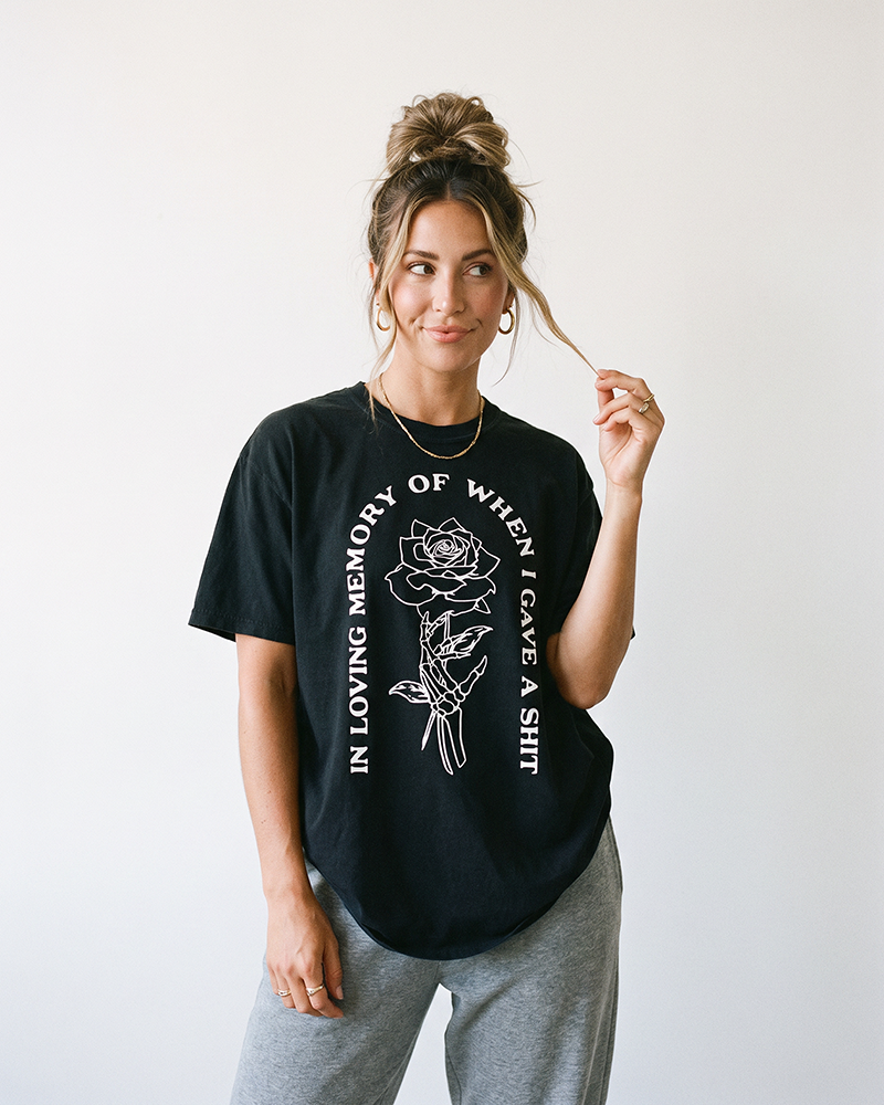 Woman wearing black In Loving Memory heavyweight graphic tee featuring skeleton hand and rose artwork