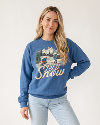 Woman wearing an Indigo blue Let It Snow midweight sweatshirt with vintage skiing and snowy mountain graphic, styled with light wash jeans.