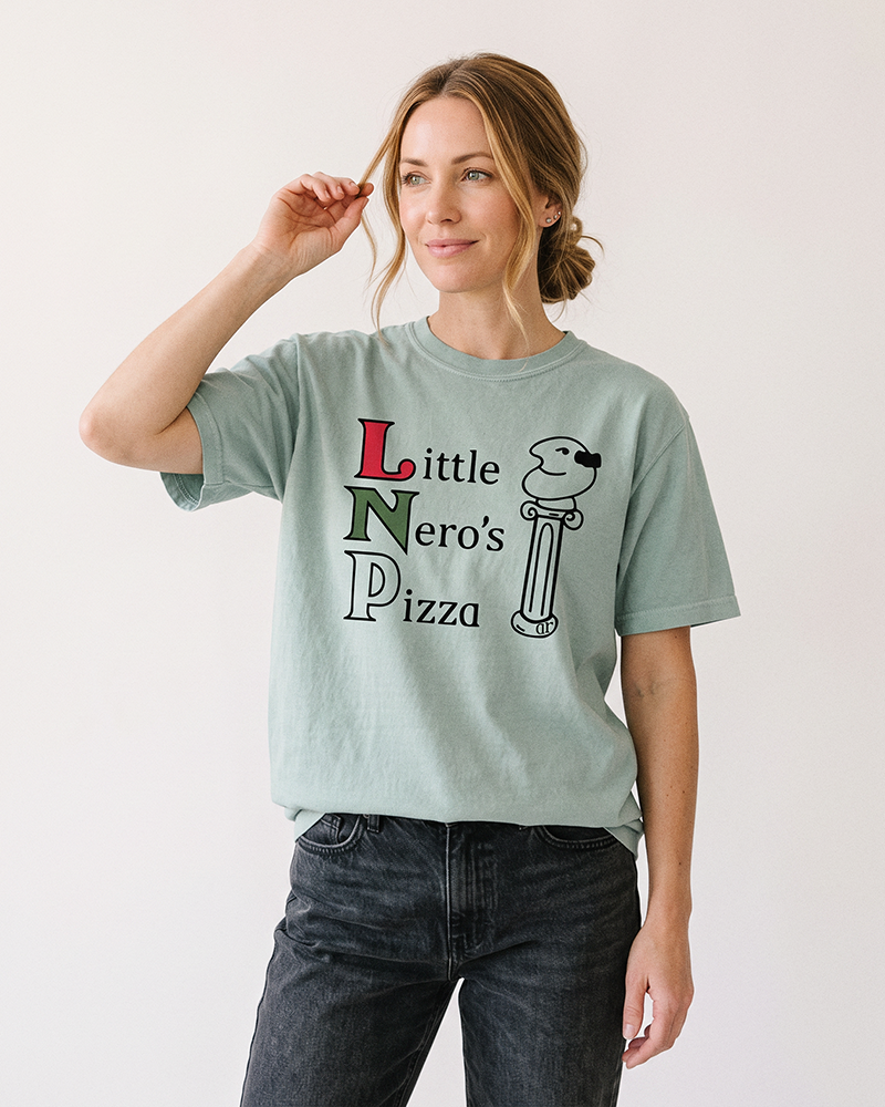 Woman wearing a Bay green Little Nero's Pizza heavyweight graphic tee with black jeans.