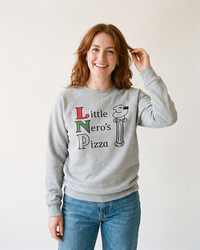 Woman wearing an athletic heather Little Nero's Pizza raglan sweatshirt with blue jeans