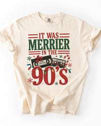 Ivory Comfort Colors heavyweight Christmas tee featuring It Was Merrier in the 90s lettering, vintage holiday cassette tapes, and colorful Christmas lights.