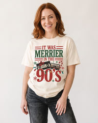 Red-haired woman wearing an Ivory It Was Merrier in the 90s heavyweight Christmas graphic tee with vintage cassette tapes and holiday lights.