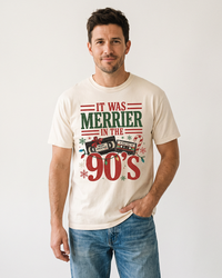 Man wearing an Ivory retro 90s Christmas T-shirt with distressed red and green lettering, cassette tapes, and blue jeans.