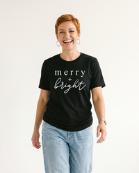 Woman wearing black Merry + Bright holiday graphic t-shirt with white lettering