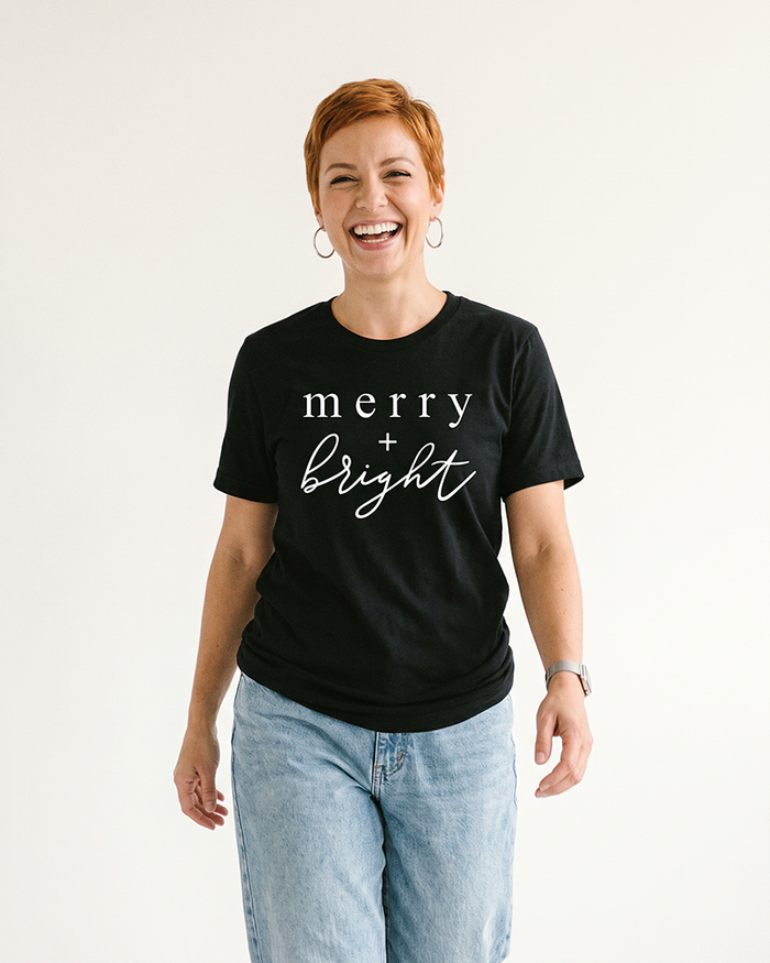 Woman wearing black Merry + Bright holiday graphic t-shirt with white lettering