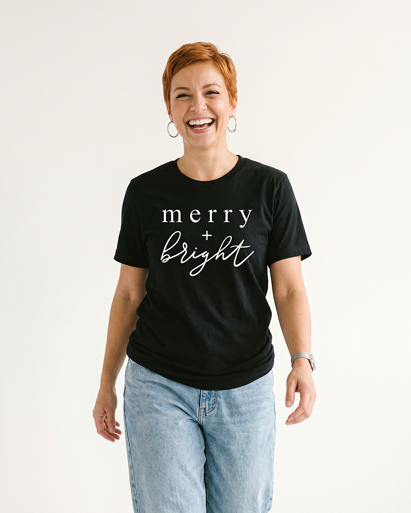 Woman wearing black Merry + Bright holiday graphic t-shirt with white lettering