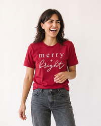 Woman wearing red Merry + Bright Christmas t-shirt with white holiday graphic