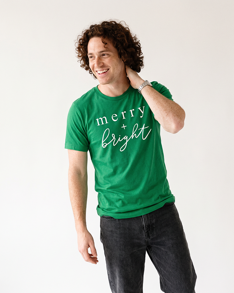 Man wearing Kelly green Merry + Bright Christmas graphic t-shirt