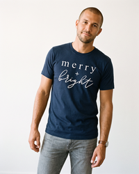 Man wearing navy Merry + Bright holiday graphic tee with white lettering