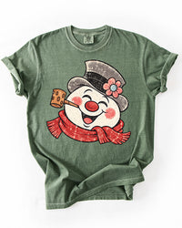 Moss green Comfort Colors heavyweight Christmas tee featuring an oversized distressed retro snowman with red scarf and top hat.